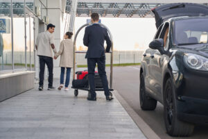 Taxis Pekin IL, Worker of airport leading trolley with suitcases behind man and woman, walking to airport entrance