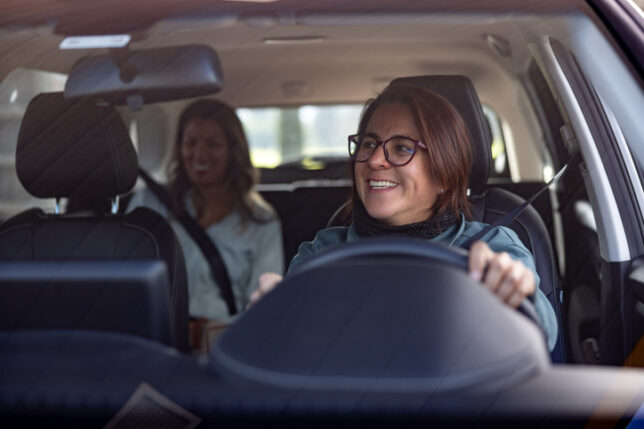 taxi cabs pekin il, Happy female crowdsourced taxi driver talking to a passenger in the back seat and looking through the rear view mirror